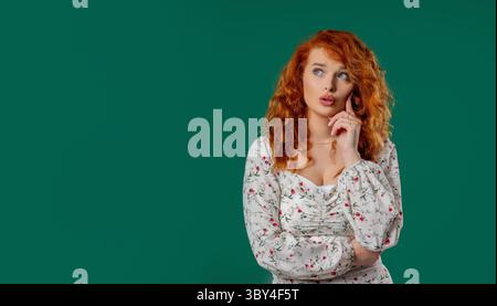 Nachdenklich um rothaarige lockige Frau auf Grün. Die Verblüffte Dame Sieht Antwort Aus Stockfoto