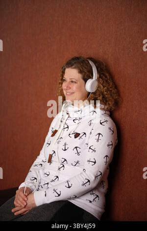 Frau im Pullover mit weißen Kopfhörern, die Musik genießt und lächelt Stockfoto