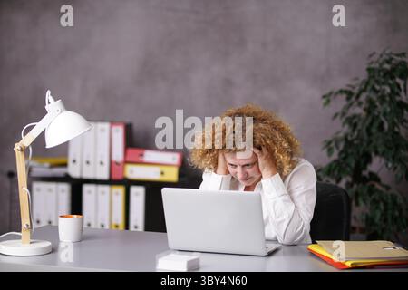 Der Sekretär sitzt am Schreibtisch vor dem Laptop, überwältigt Stockfoto