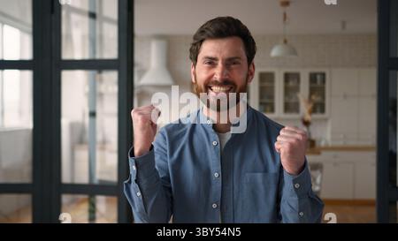 Glücklicher glücklicher Kaukasier Mann Gewinner Dad lächelnd geballte Fäuste männlicher Gewinn Freude zu Hause Erfolg Aufregung glückliche Eltern schreien ja Gefühl Stockfoto