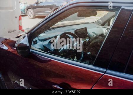 Cremona, Italien - 1. April 2025 Sonnenlicht reflektiert vom burgunderroten Nissan Juke, der neben einem weißen Van geparkt ist und das Lenkrad und den Dashbo hervorhebt Stockfoto