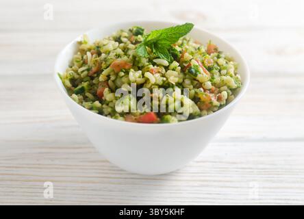 Orientalischer Salat Tabbouleh in einer weißen Schüssel auf einem Holztisch. Konzept der traditionellen libanesischen oder syrischen Küche. Vegetarische oder vegane Gerichte. Selektiver lichtwellenleiter Stockfoto