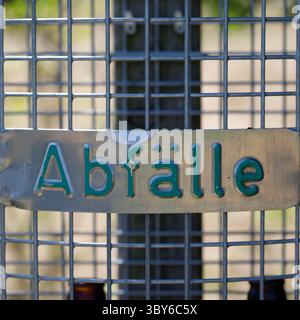 Nahaufnahme eines Abfallbehälters aus Metall. Der Schwerpunkt liegt auf dem Schild mit der Aufschrift „Abfall“ in grünen Buchstaben. Die Buchse hat ein Drahtgeflecht. Stockfoto
