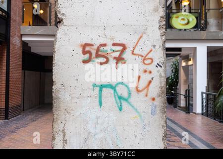 Graffiti schmücken eine Betonsäule in einem belebten Stadtrand und spiegeln urbane Kunst und Kultur zwischen Ziegelboden und malerischen Balkonen wider. Stockfoto
