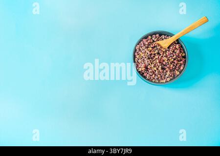 Oben rechts Schüssel getrocknete Sichuan Pfefferspulen mit winzigem Holzlöffel auf lebendigem himmelblauem Hintergrund, minimaler kulinarischer Flachlagebereich mit großem Kopierraum Stockfoto