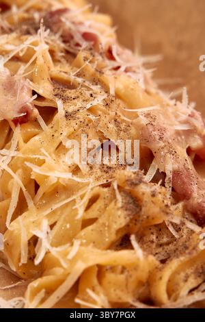 Herzhafte Carbonara-Pasta mit knusprigem Speck, bestreut mit Parmesan und zerbrochenem schwarzem Pfeffer, kreieren ein köstliches italienisches Gericht voller Zutaten Stockfoto