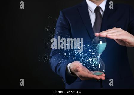 Die Zeit wird knapp. Sanduhr löst sich in den Händen des Menschen auf schwarzem Hintergrund auf, Nahaufnahme Stockfoto