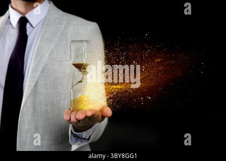 Die Zeit wird knapp. Sanduhr löst sich in der Hand des Menschen auf schwarzem Hintergrund auf, Nahaufnahme Stockfoto