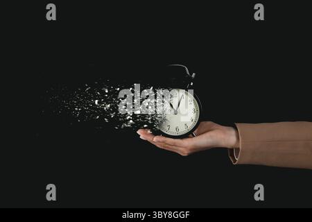 Die Zeit wird knapp. Wecker löst sich in der Hand der Frau auf, vor schwarzem Hintergrund, Nahaufnahme Stockfoto