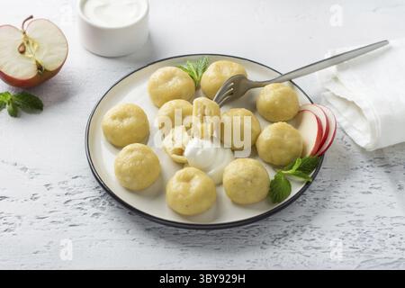 Essen, vegetarische glutenfreie, gedämpfte Lazy-Knödel mit Apfelfüllung auf einem weißen Teller, dekoriert mit Minze, umgeben von einem halben Apfel und saurem Crea Stockfoto