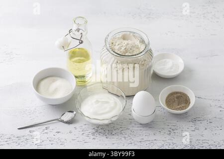 Lebensmittel, Zutaten zum hausgemachten Backen: Ei, Sauerrahm oder Joghurt, Zucker, Vanillezucker, Mehl, Pflanzenöl, Backpulver, Salz auf hellblauem Rücken Stockfoto