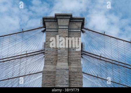 Majestätische Steinsäule und Kabel der Brooklyn Bridge, ein berühmtes architektonisches Wunder, unter einem dramatischen bewölkten Himmel. Stockfoto