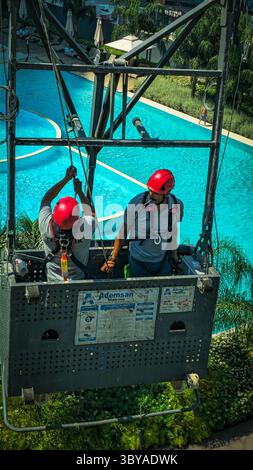 Zwei Bauarbeiter arbeiten im Freien zwei Bauarbeiter mit Helmen und Sicherheitsgurten stehen auf einer hängenden Wiege in einem Hochhaus und arbeiten draußen an einem sonnigen Tag mit einer Stadtlandschaft im Hintergrund Izmir Konak Türkei Copyright: xx 20250719 111719 Stockfoto