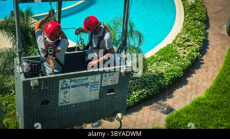 Zwei Bauarbeiter arbeiten im Freien zwei Bauarbeiter mit Helmen und Sicherheitsgurten stehen auf einer hängenden Wiege in einem Hochhaus und arbeiten draußen an einem sonnigen Tag mit einer Stadtlandschaft im Hintergrund Izmir Konak Türkei Copyright: xx 20250719 111711 Stockfoto