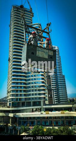 Zwei Bauarbeiter arbeiten im Freien zwei Bauarbeiter mit Helmen und Sicherheitsgurten stehen auf einer hängenden Wiege in einem Hochhaus und arbeiten draußen an einem sonnigen Tag mit einer Stadtlandschaft im Hintergrund Izmir Konak Türkei Copyright: xx 20250719 112041 Stockfoto