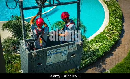 Zwei Bauarbeiter arbeiten im Freien zwei Bauarbeiter mit Helmen und Sicherheitsgurten stehen auf einer hängenden Wiege in einem Hochhaus und arbeiten draußen an einem sonnigen Tag mit einer Stadtlandschaft im Hintergrund Izmir Konak Türkei Copyright: xx 20250719 111708 Stockfoto