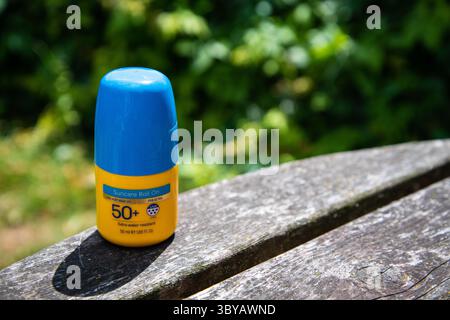Sonnencreme mit gelbem Faktor 50+ und blauem Deckel, bei hellem Sonnenschein auf einem hölzernen Gartentisch platziert, was an Sommer, Sonnenschutz und Freizeit im Freien erinnert Stockfoto