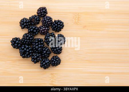 Blick von oben auf frische Brombeeren auf einem rustikalen Holzbrett mit Textur, Farbkontrast und natürlicher Anordnung in minimaler Essenszusammensetzung Stockfoto
