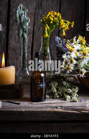Ätherisches Öl in Glasflasche mit Wildblumen und Kerzen Stockfoto