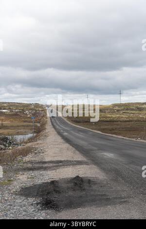 Teriberka, Russland - 13. Juni 2025: Eine abgelegene Straße zieht sich durch die arktische Tundra-Landschaft mit spärlichem Verkehr und Versorgungsmasten entlang des Weges Stockfoto