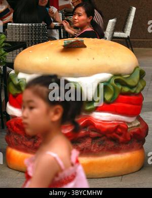 28. Juni 2013, PEKING, CHINA: Eine Chinesin isst am 28. Juni 2013 vor einem neuen Burger King Fast Food Restaurant in der Innenstadt von Peking zu Mittag. Chinesische Gesundheitsbeamte machen das Aufkommen einer im ganzen Land boomenden westlichen Fast-Food-Revolution als Hauptursache für eine wachsende Adipositas-Krise in China verantwortlich. Adipositas in China, insbesondere bei Kindern, ist zu einem wachsenden Gesundheitsrisiko geworden, das nicht nur die Gesundheit künftiger Generationen ernsthaft beeinträchtigen wird, sondern auch eine schwere wirtschaftliche Belastung für das Land darstellt. (Bild: © Stephen Shaver/ZUMA Press Wire) Stockfoto