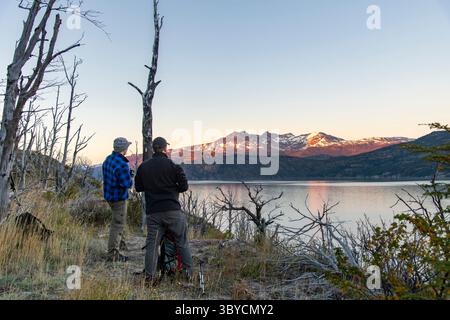 Zwei Wanderer auf der W-Trek-Wanderroute entlang des Lago Grey Sees im Torres del Paine Nationalpark, Chile beobachtet den Sonnenaufgang mit dem ersten Licht auf Schnee bedeckt Stockfoto