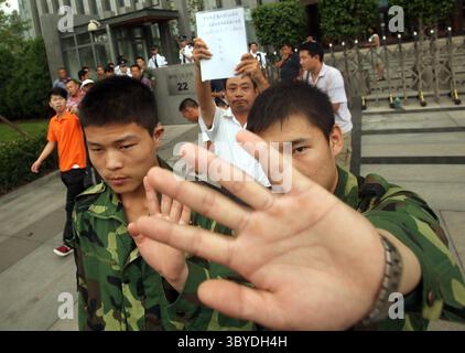 14. Juli 2010, PEKING, CHINA: Chinesische Sicherheitsjournalisten sollen am 14. Juli 2010 die Front des chinesischen Ölriesen PetroChina verlassen, während eine kleine Gruppe von Arbeitern vor dem Gebäude in Peking protestiert. China hat in den letzten Wochen eine zunehmende Zahl von Arbeiterprotesten erlebt, von Streiks in einem Honda-Werk bis hin zu düsteren Berichten über Selbstmord im riesigen Foxconn-Komplex. (Bild: © Stephen Shaver/ZUMA Press Wire) Stockfoto