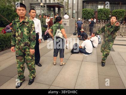 14. Juli 2010, PEKING, CHINA: Chinesische Sicherheitsjournalisten sollen am 14. Juli 2010 die Front des chinesischen Ölriesen PetroChina verlassen, während eine kleine Gruppe von Arbeitern vor dem Gebäude in Peking protestiert. China hat in den letzten Wochen eine zunehmende Zahl von Arbeiterprotesten erlebt, von Streiks in einem Honda-Werk bis hin zu düsteren Berichten über Selbstmord im riesigen Foxconn-Komplex. (Bild: © Stephen Shaver/ZUMA Press Wire) Stockfoto