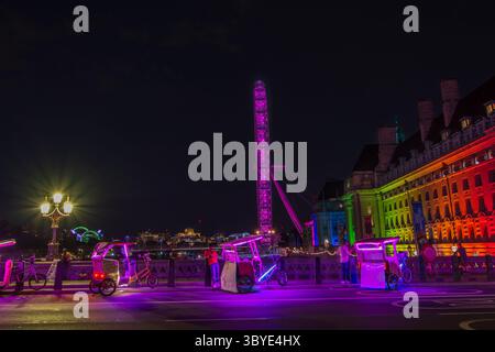 Das London Eye bei Nacht mit Tuk-Tuk-Fahrzeugen, die auf der Westminster Bridge, London, England, Großbritannien, geparkt sind. Es ist das höchste freitragende Rad der Welt. Stockfoto