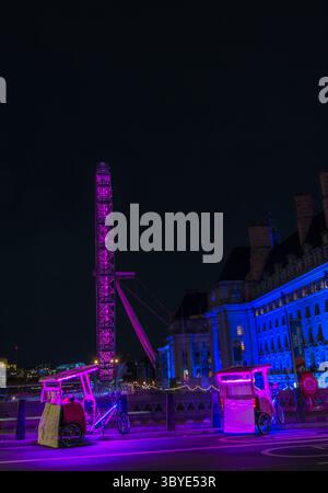 Das London Eye bei Nacht mit Tuk-Tuk-Fahrzeugen, die auf der Westminster Bridge, London, England, Großbritannien, geparkt sind. Es ist das höchste freitragende Rad der Welt. Stockfoto