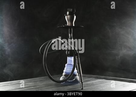 Shisha auf Holztisch mit Rauch vor schwarzem Hintergrund Stockfoto