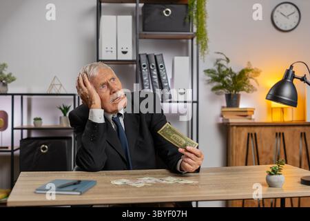 Kaukasischer Senior-Geschäftsmann Freelancer zählt Bargeld zu wenig Geld. Finanzkrise. Konkurs. Armut und Elend. Großvater im Anzug sitzt am Tisch im Büro. Stockfoto