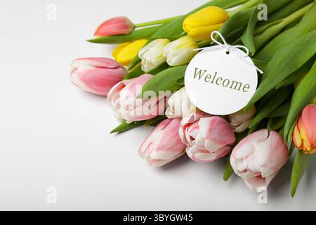 Willkommenskarte und Tulpen auf weißem Tisch, Nahaufnahme Stockfoto