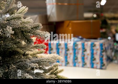 Ein wunderschön mattierter Weihnachtsbaumzweig im Vordergrund mit einem weichen Fokus auf einem Stapel ordentlich gewickelter Geschenke, die an das warme und fröhliche erinnern Stockfoto