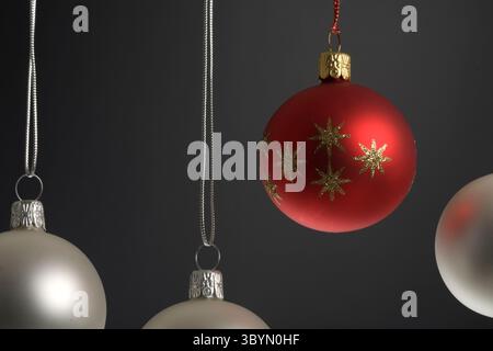 Rote Weihnachtskugel im Fokus mit drei Silber nebenan auf schwarzem Hintergrund Stockfoto