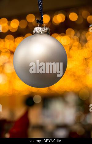 Silberne Weihnachtskugel hängt mit verschwommenen Weihnachtslichtern im Hintergrund Stockfoto