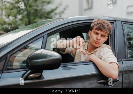 Trauriger junger Fahrer, der im Auto die Daumen nach unten zeigt. Schlechter Kundenservice durch die Werkstatt Stockfoto