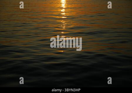 Goldenes Sonnenlicht reflektiert bei Sonnenuntergang auf der ruhigen Wasseroberfläche und schafft eine friedliche und ruhige Atmosphäre. Die warmen Töne wecken ein Gefühl der Ruhe A Stockfoto
