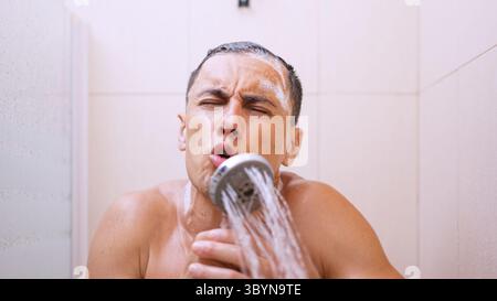 Mann singt unter der Dusche mit Duschkopf als Mikrofon Stockfoto