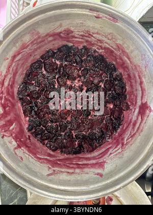 Nahaufnahme einer runden, metallischen Schüssel mit dunklen, rötlich-violetten Kirschen, die wie gekocht oder gedünstet für Marmelade und Tortenfüllung aussehen. Stockfoto
