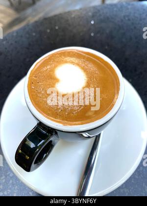 Nahaufnahme einer Tasse Kaffee oder Espresso von oben auf einer weißen Untertasse mit rötlich-brauner Crema und einem herzförmigen Stück weißer Milch. Stockfoto
