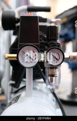 Nahaufnahme eines Luftkompressors mit Schwerpunkt auf den Manometern und dem Regler. Wird in Werkstätten, Garagen oder industriellen Umgebungen verwendet. Stockfoto