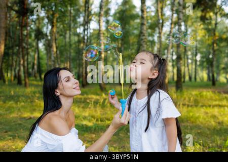 Mutter und Tochter genießen im Sommerwald Wasserblasen im Freien glückliche Kindheit, Familienspaß und fröhliche Momente in der Natur Stockfoto