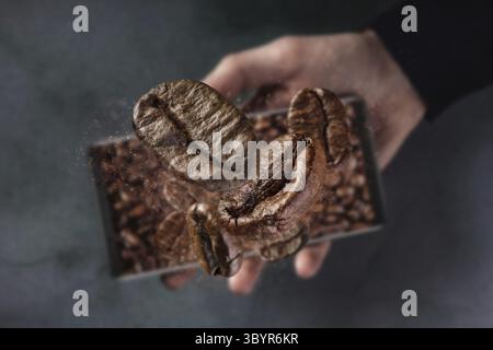 Handy und frisch gerösteten fallenden Kaffeebohnen Konzept mit betonierten Hintergrund. Mann, der Phon hält, ohne Kaffeebohnen zu fliegen Stockfoto