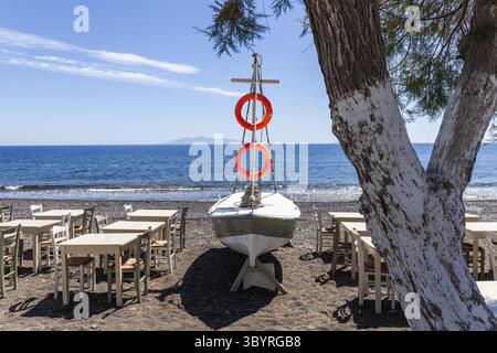 Restauranttische und Boot am Strand, hinter Anafi Island, Kamari, Santorini Island, Kykladen, Griechenland Stockfoto