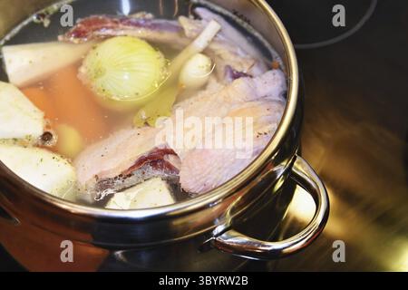 Hausgemachte Hühnersuppe - Brühe. Topf auf dem Herd in der Küche mit Zutaten zum Kochen Stockfoto