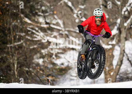 Radfahrer springt Fat Bike im Schnee während des Montpelier, VT, Winterfest Fat Bike Rennen. Stockfoto