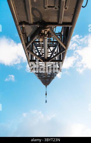 Ein Pfeil mit einem Haken eines Hafenkrans gegen einen blauen Himmel mit Wolken. Ansicht von unten. Stockfoto