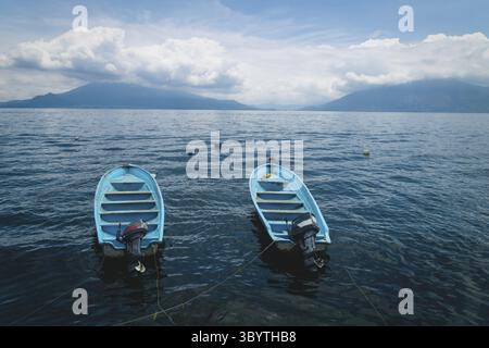 Zwei parallel schwimmende blaue Boote auf dem dunkelblauen See Atitlan mit Blick auf die Vulkane San Pedro und Toliman in Santa Cruz la Laguna, Guatemala Stockfoto