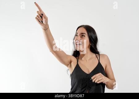 Aufgeregte junge Frau, die mit dem Finger auf etwas Interessantes auf weißem Hintergrund zeigt Stockfoto